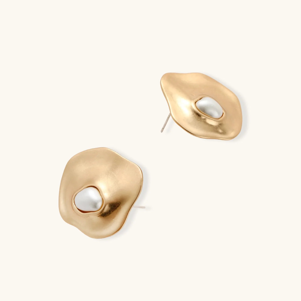 Gold organic-shaped stud earrings with white pearl centers and flowing curves on neutral background.