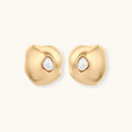 Gold organic-shaped stud earrings with white pearl centers and flowing curves on neutral background.