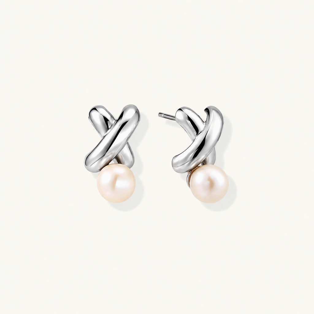 Rhodium-plated silver earrings with twisted X design and freshwater pearl drops on beige background