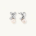 Rhodium-plated silver earrings with twisted X design and freshwater pearl drops on beige background