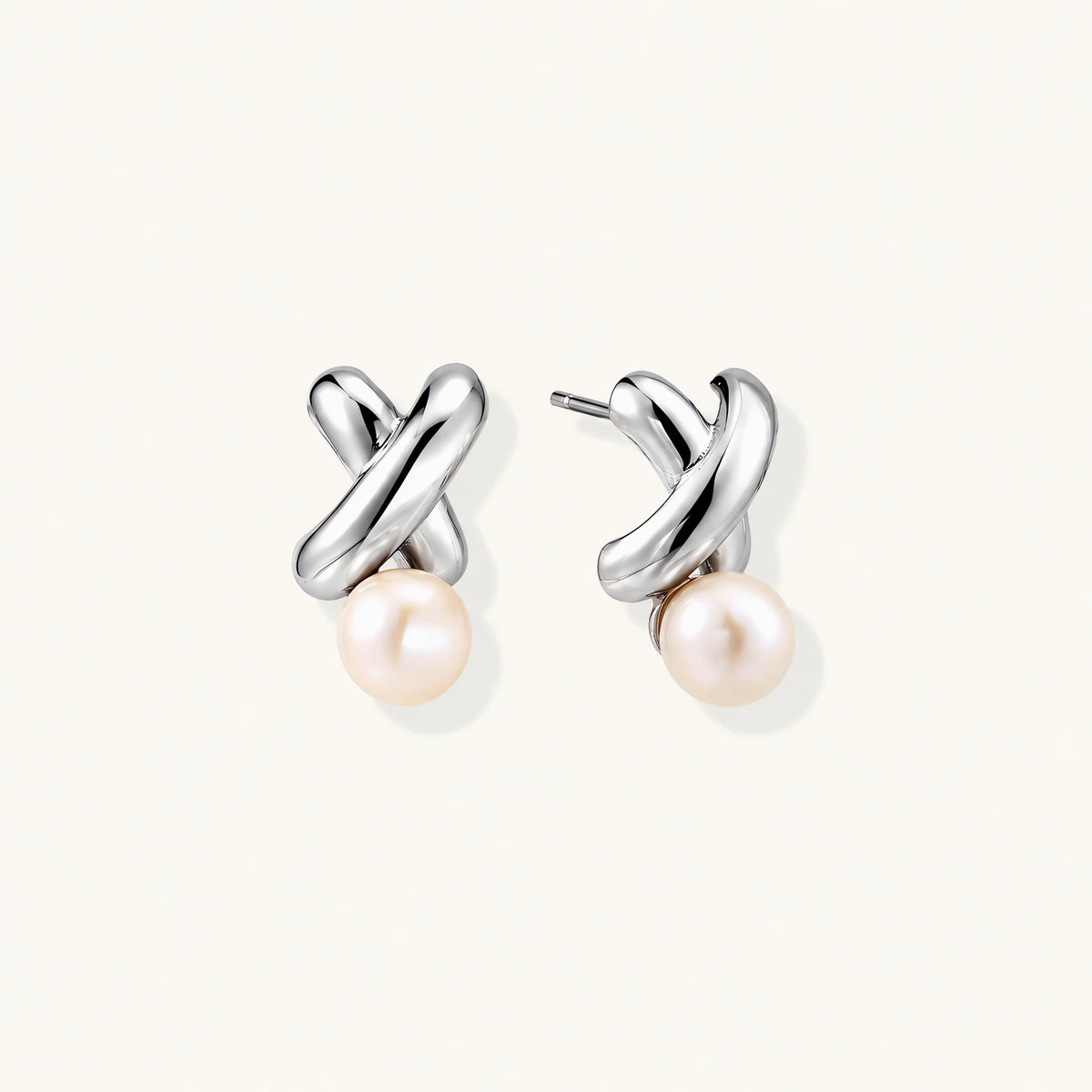 Rhodium-plated silver earrings with twisted X design and freshwater pearl drops on beige background