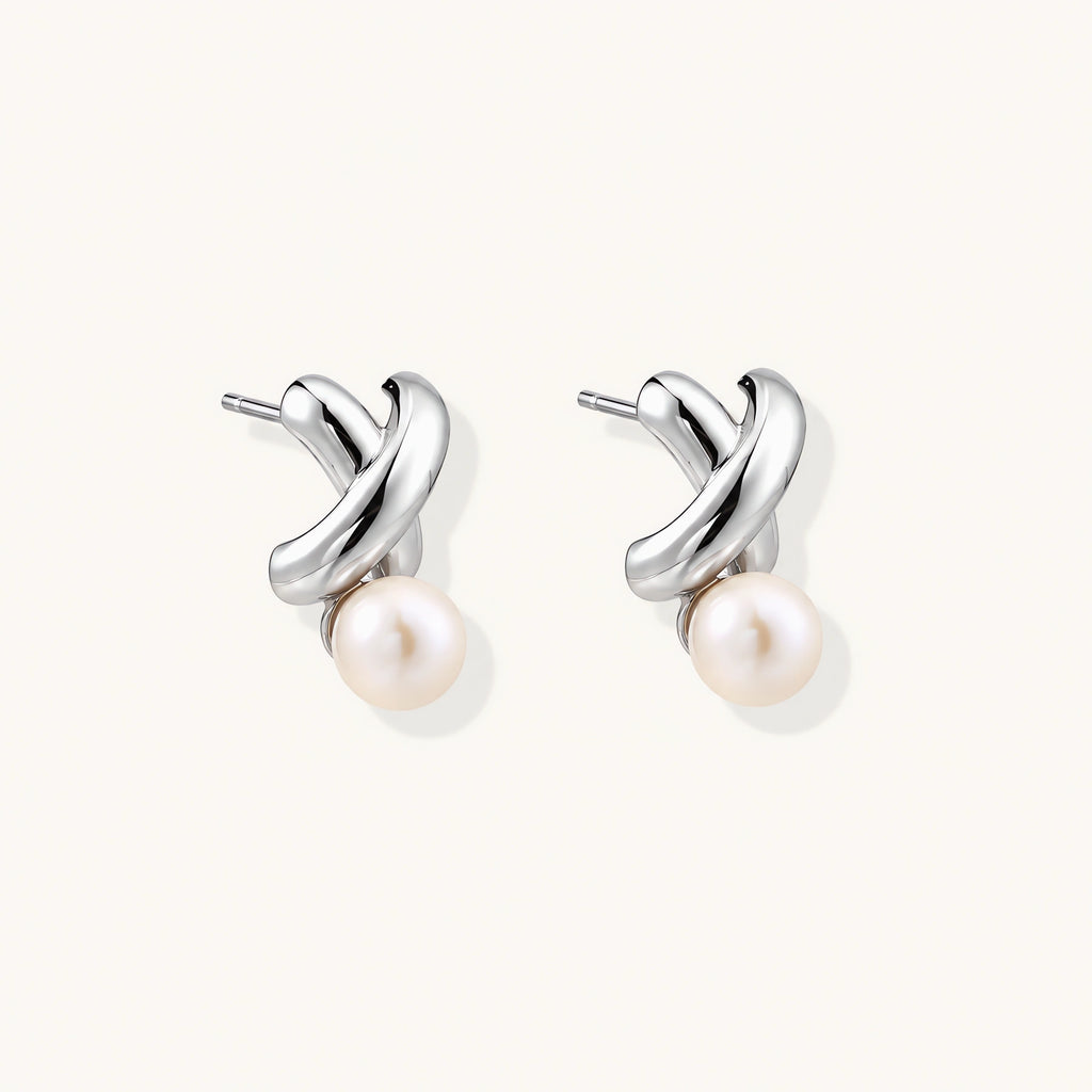 Rhodium-plated silver earrings with twisted X design and freshwater pearl drops on beige background