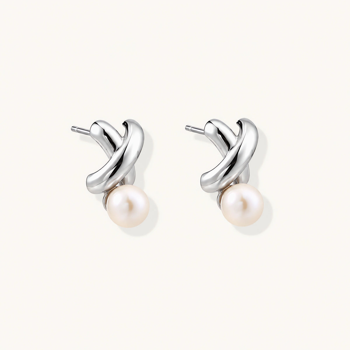 Rhodium-plated silver earrings with twisted X design and freshwater pearl drops on beige background