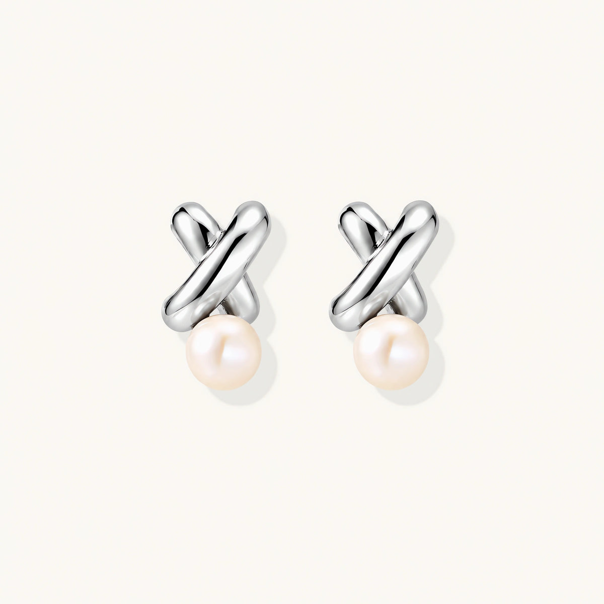 Rhodium-plated silver earrings with twisted X design and freshwater pearl drops on beige background