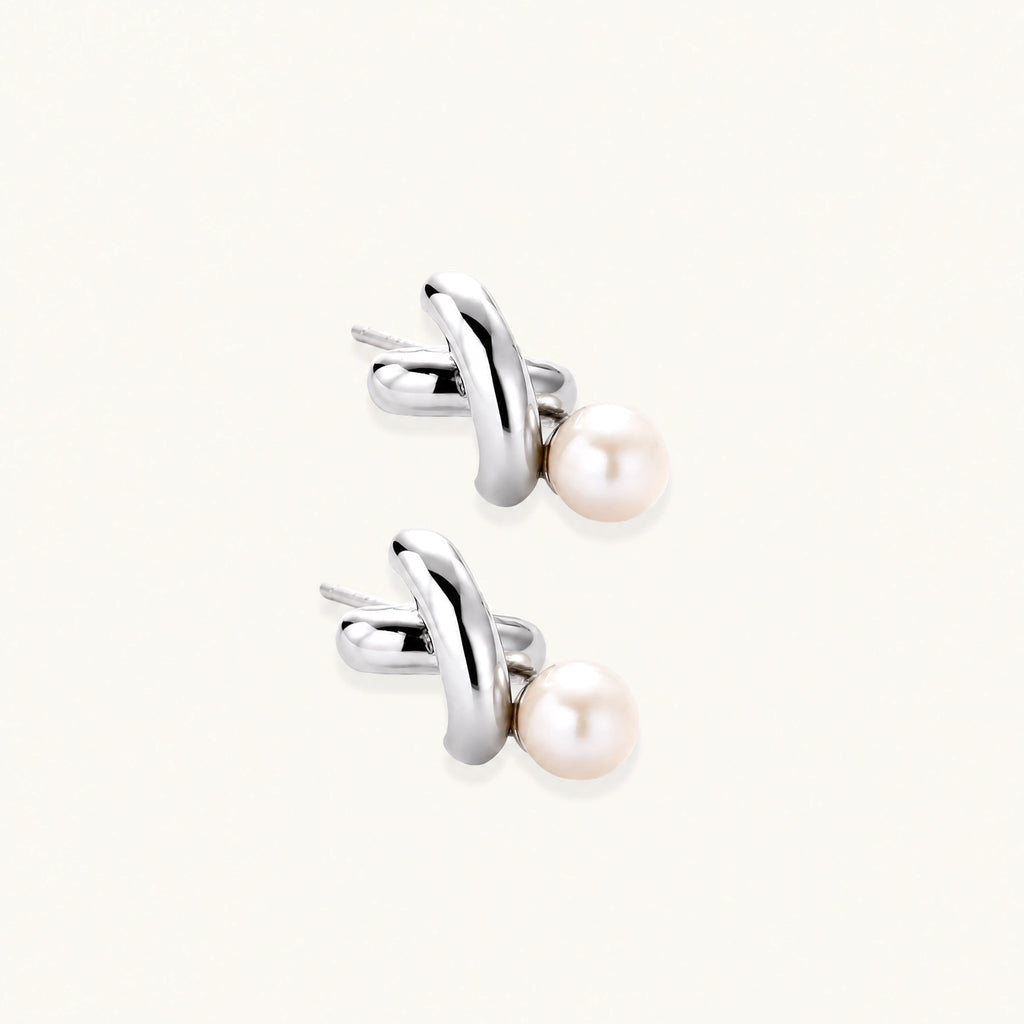 Rhodium-plated silver earrings with twisted X design and freshwater pearl drops on beige background