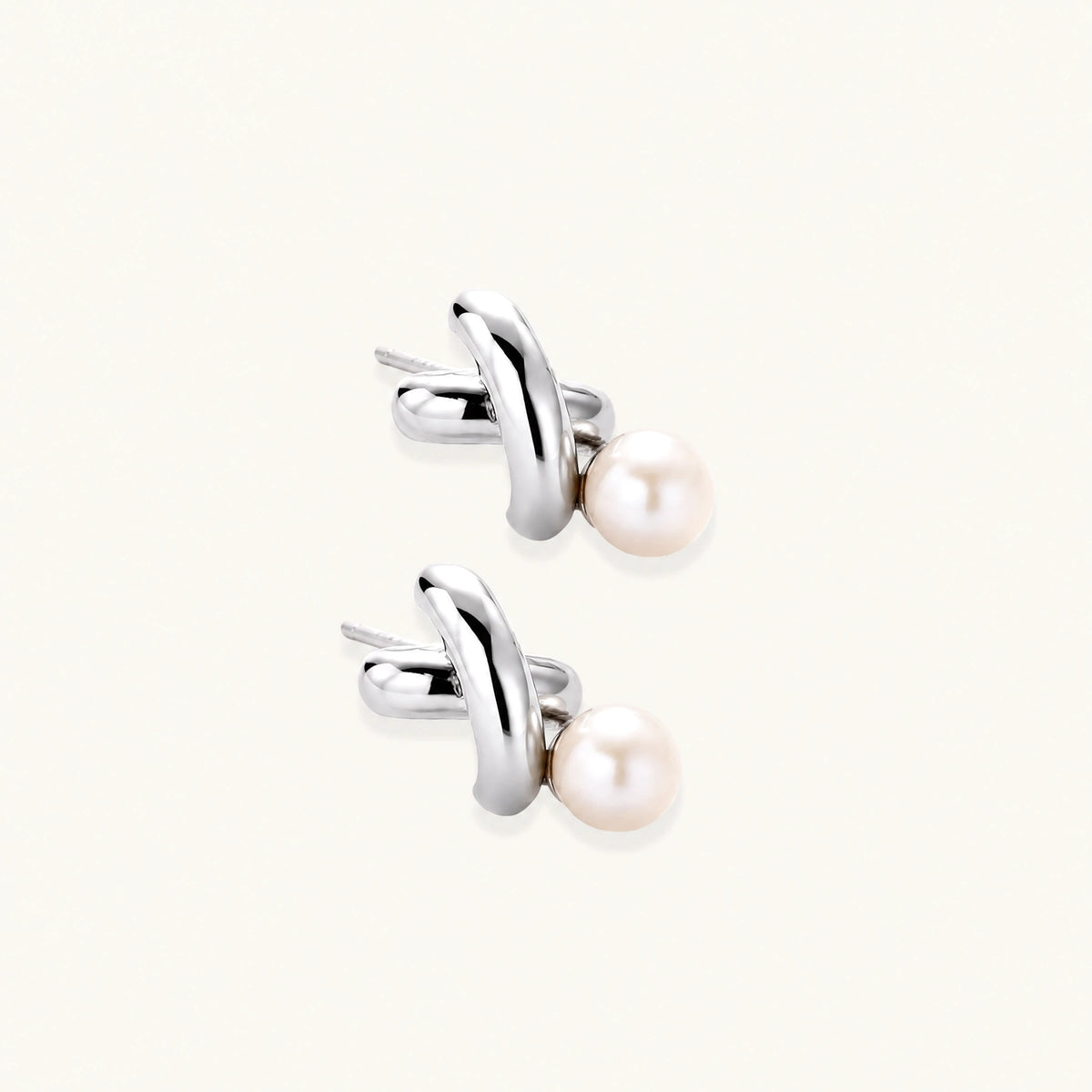 Rhodium-plated silver earrings with twisted X design and freshwater pearl drops on beige background