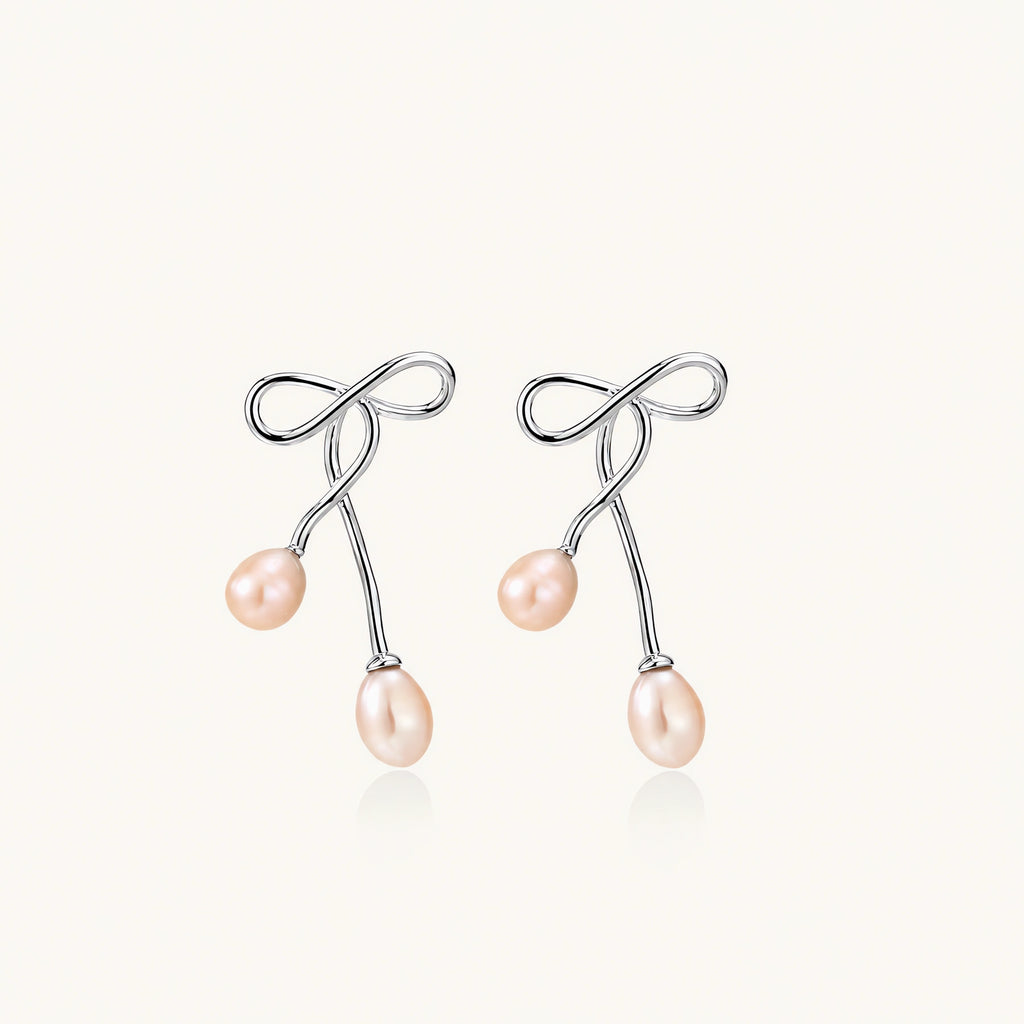Rhodium-plated silver earrings with organic vine curves and two peachy freshwater pearls on cream background
