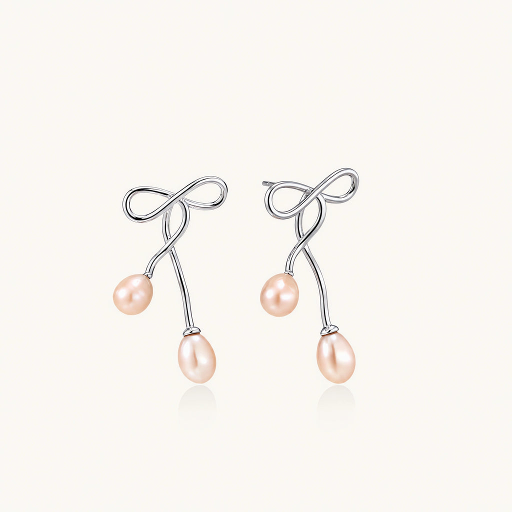 Rhodium-plated silver earrings with organic vine curves and two peachy freshwater pearls on cream background