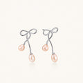 Rhodium-plated silver earrings with organic vine curves and two peachy freshwater pearls on cream background