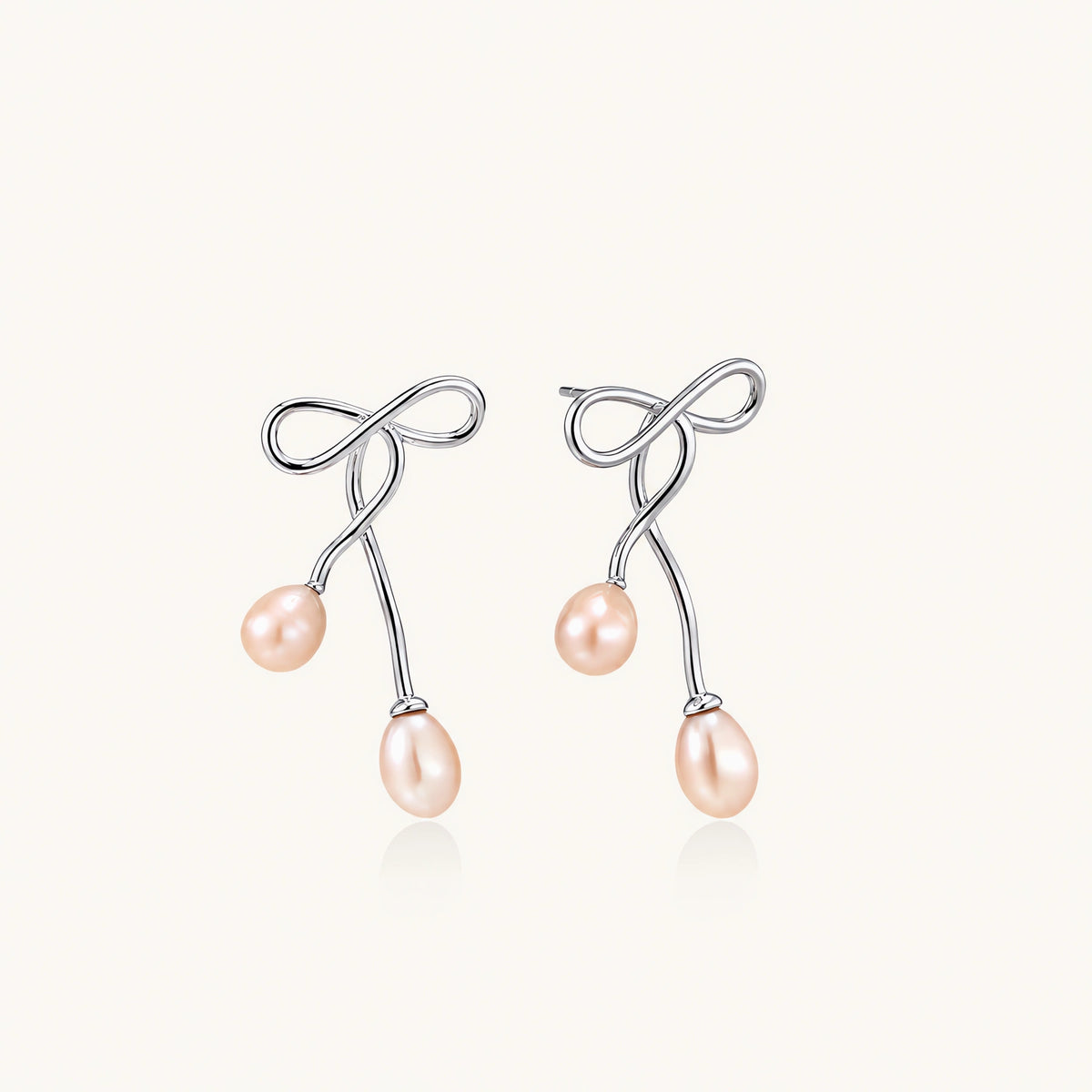 Rhodium-plated silver earrings with organic vine curves and two peachy freshwater pearls on cream background
