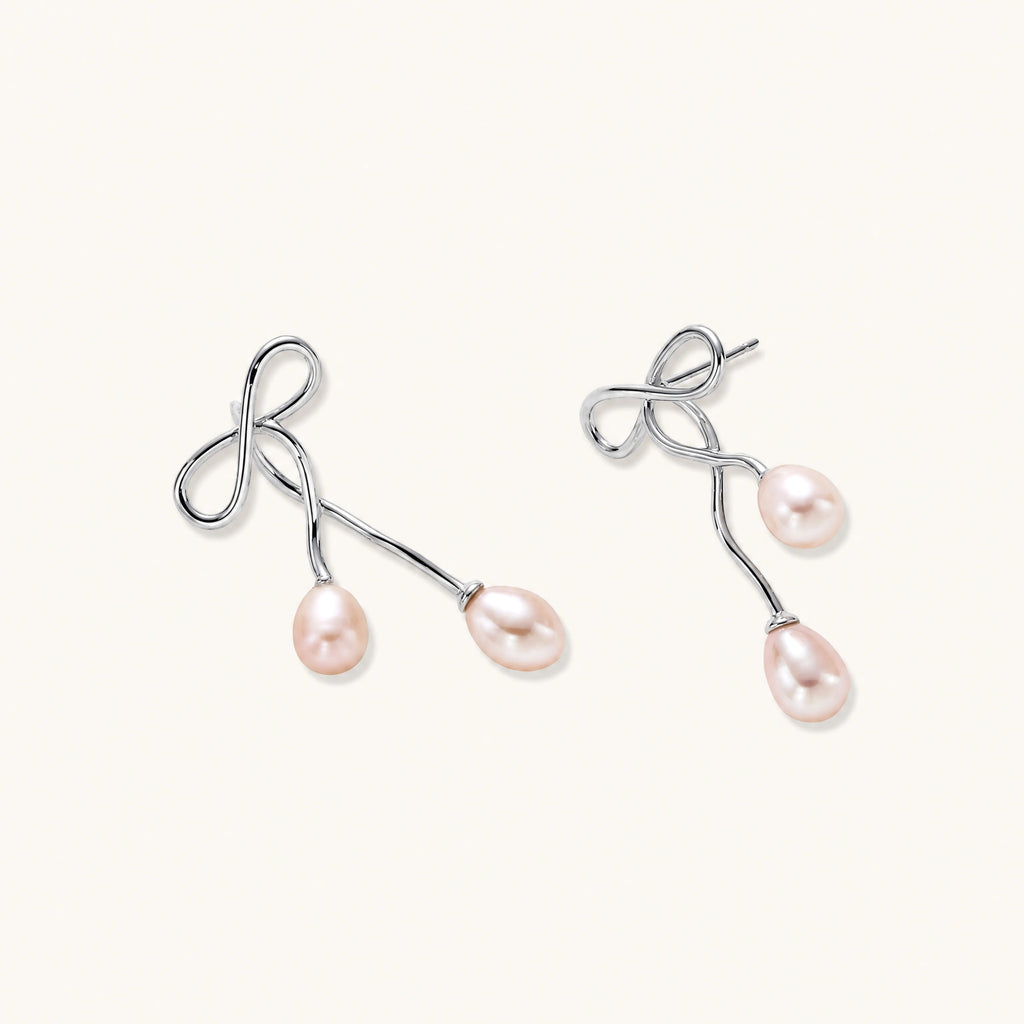 Rhodium-plated silver earrings with organic vine curves and two peachy freshwater pearls on cream background
