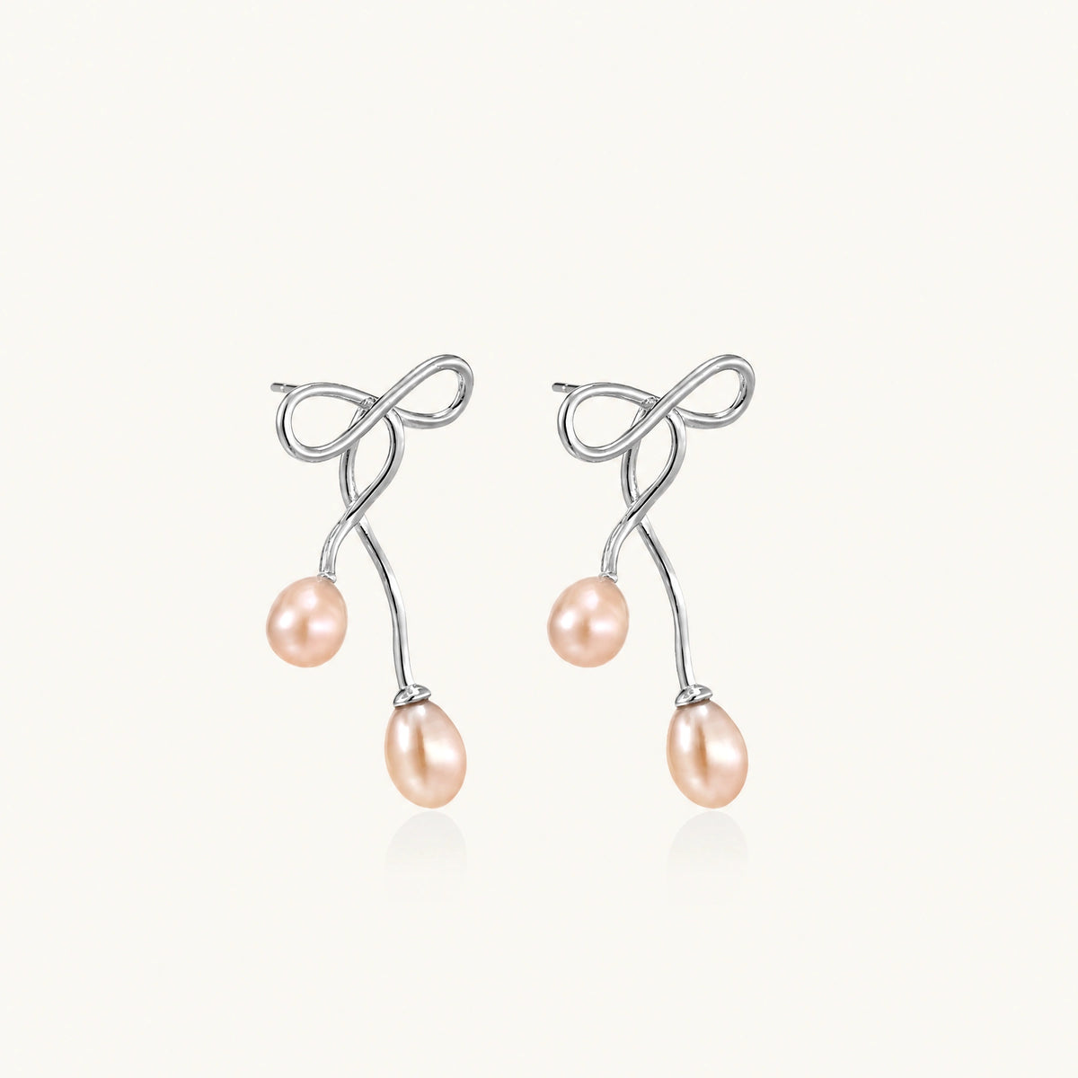 Rhodium-plated silver earrings with organic vine curves and two peachy freshwater pearls on cream background