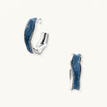 Silver huggie hoops with blue denim fabric inlay strip and polished white gold plated finish on cream background.