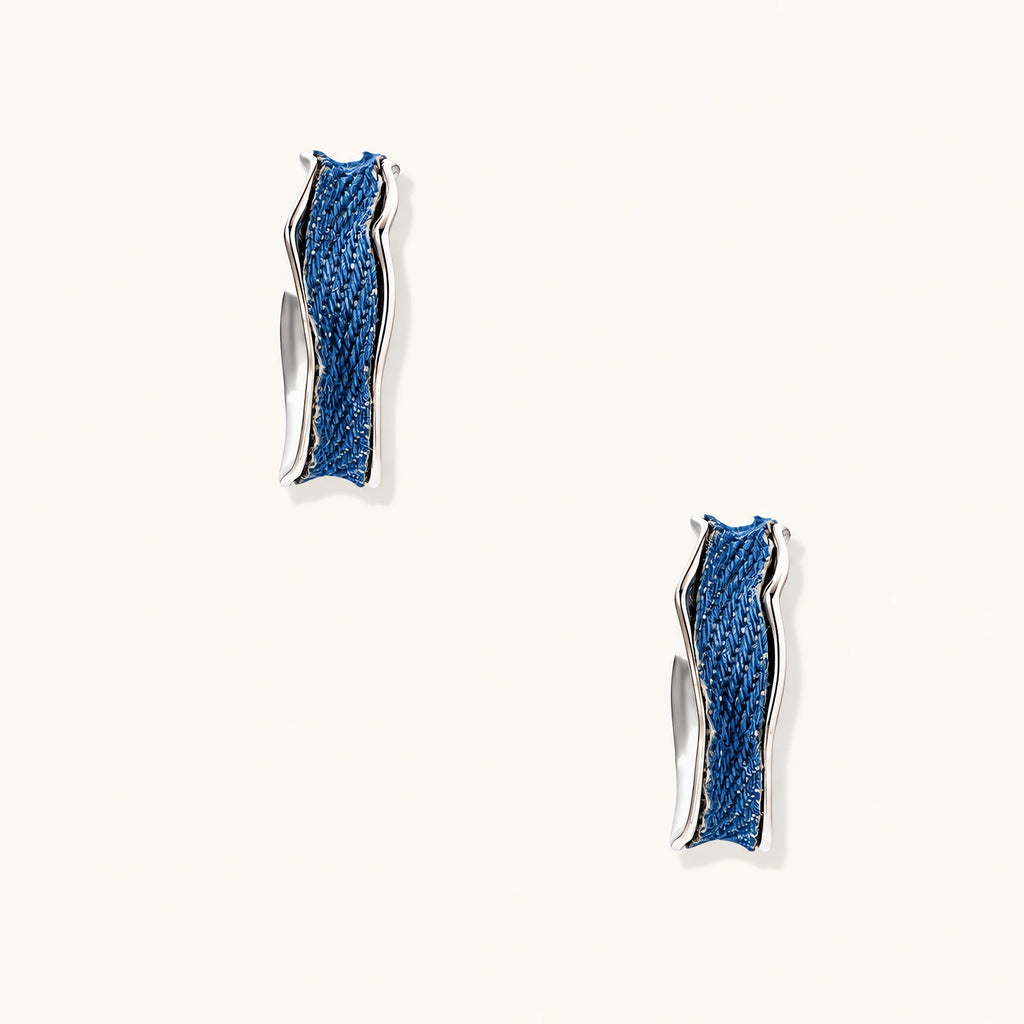 Silver huggie hoops with blue denim fabric inlay strip and polished white gold plated finish on cream background.
