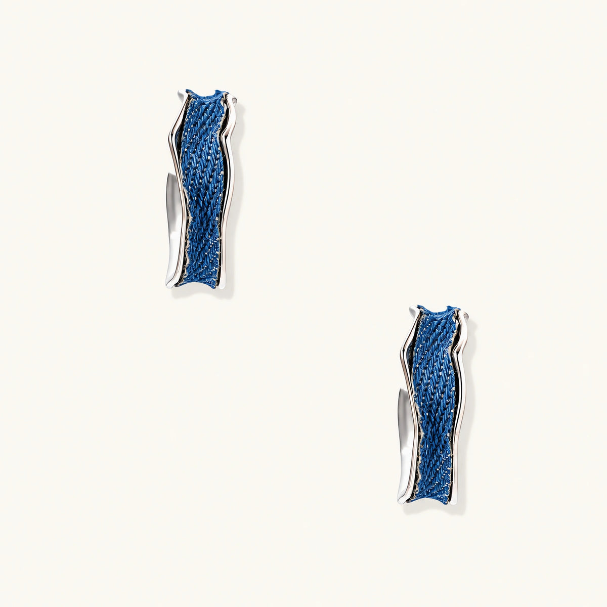 Silver huggie hoops with blue denim fabric inlay strip and polished white gold plated finish on cream background.