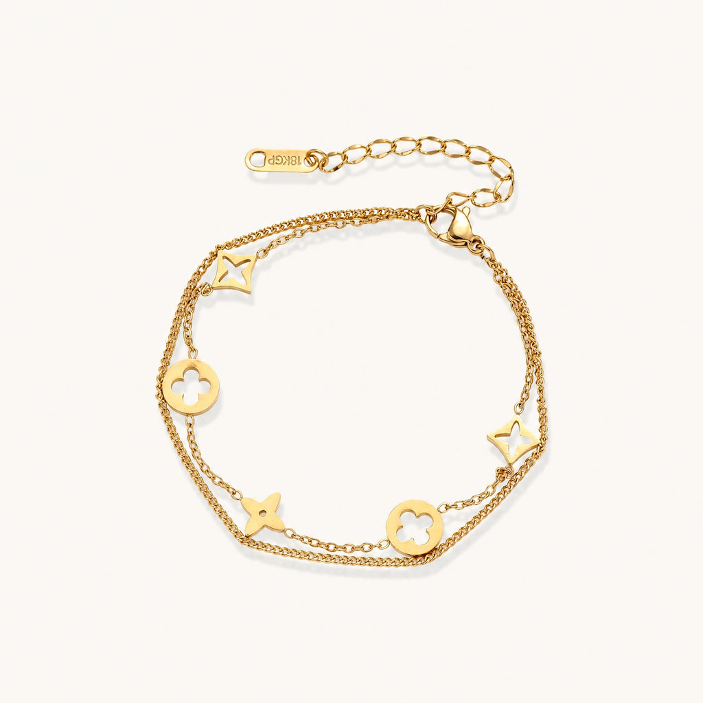 Double-layer gold-plated bracelet with quatrefoil and star charms on cream background, 18K gold finish.