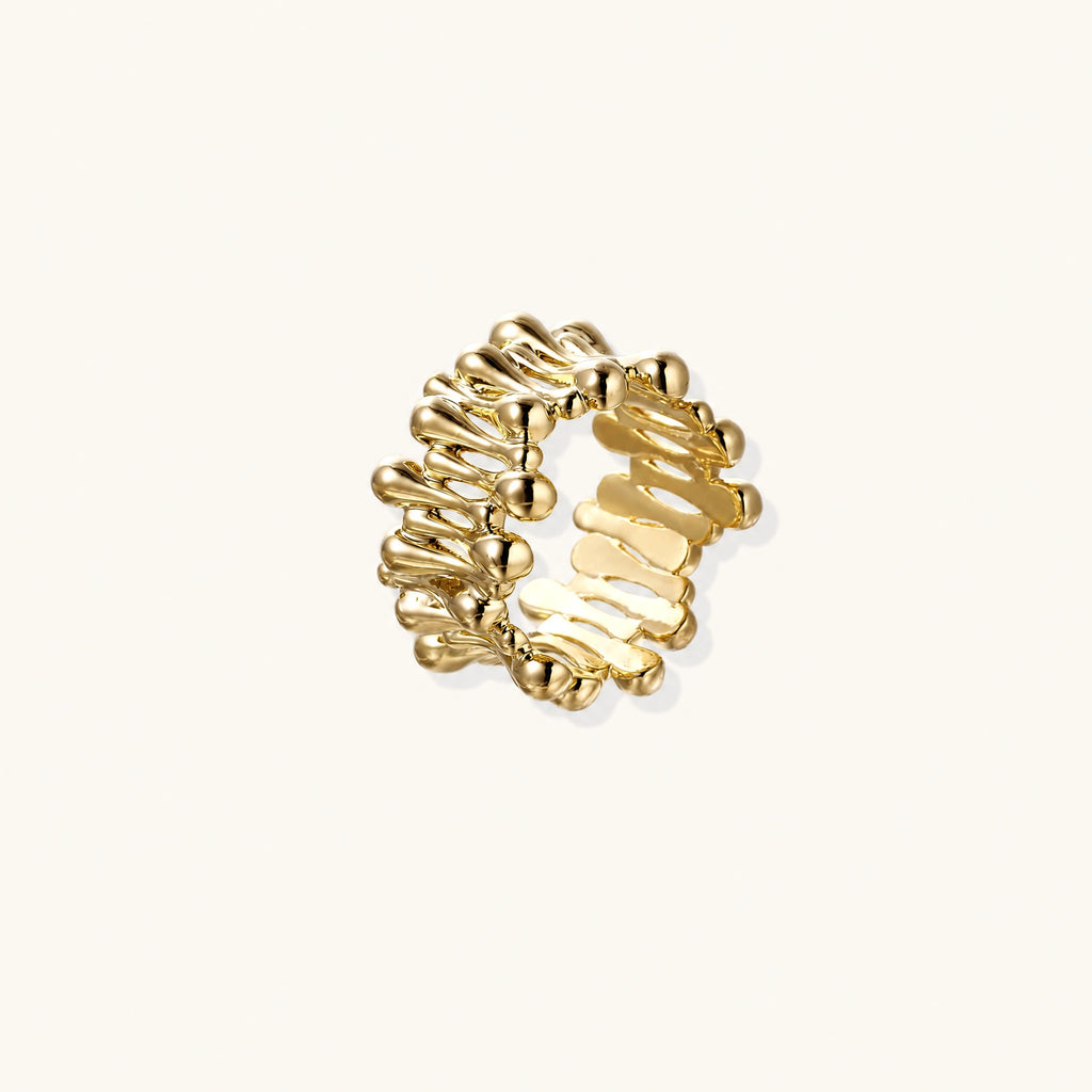 Gold-plated brass ring with sculptural petal-like elements in a wide band design on beige background