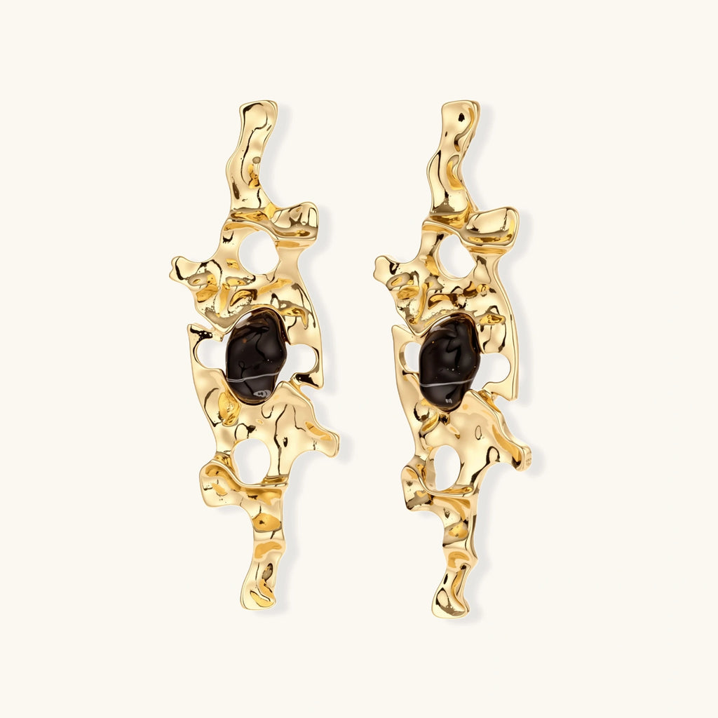 Gold-toned abstract dangle earrings with flowing cutout design and dark resin center accents on white background.
