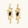Gold-toned abstract dangle earrings with flowing cutout design and dark resin center accents on white background.