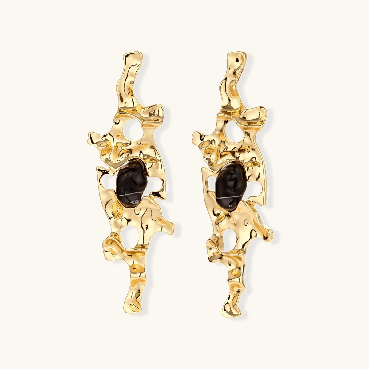 Gold-toned abstract dangle earrings with flowing cutout design and dark resin center accents on white background.