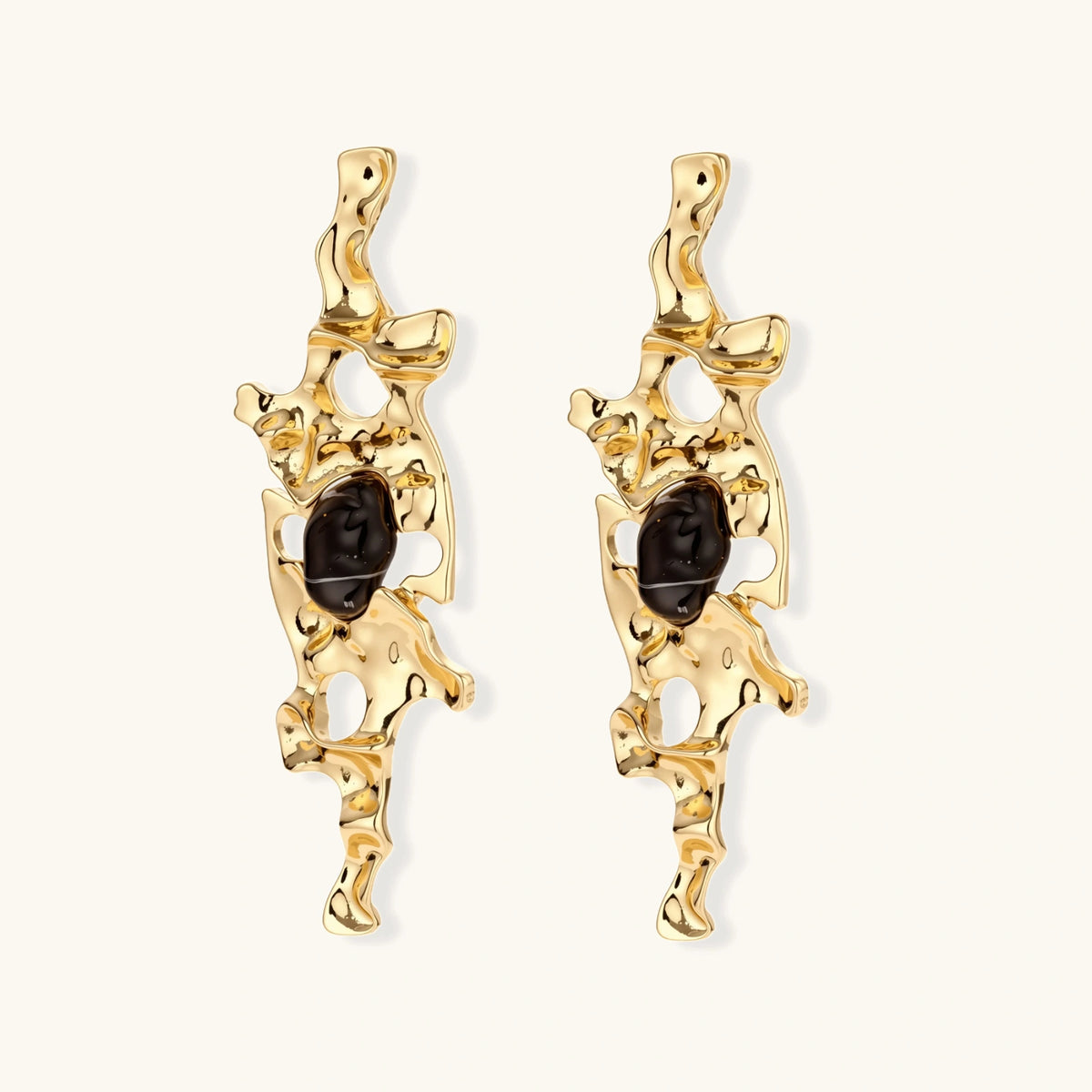 Gold-toned abstract dangle earrings with flowing cutout design and dark resin center accents on white background.