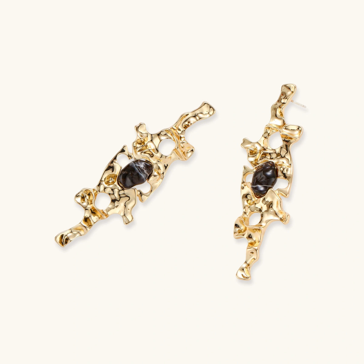 Gold-toned abstract dangle earrings with flowing cutout design and dark resin center accents on white background.
